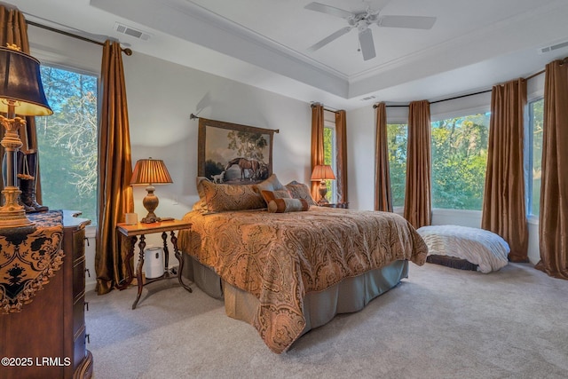 bedroom featuring light carpet, a tray ceiling, ornamental molding, and ceiling fan