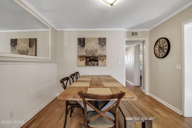 dining space with hardwood / wood-style floors, crown molding, and a textured ceiling