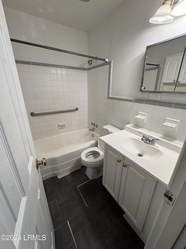 full bathroom with tile walls, vanity, tiled shower / bath, tile patterned floors, and toilet