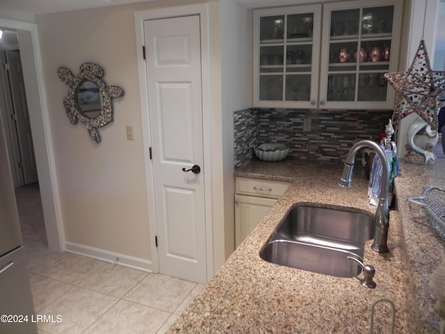 kitchen with light stone countertops, sink, light tile patterned floors, and decorative backsplash