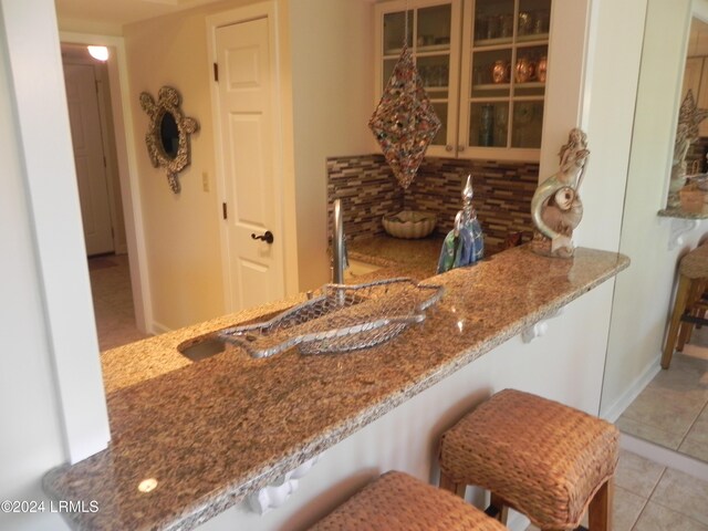 kitchen featuring a breakfast bar, light tile patterned floors, backsplash, and kitchen peninsula