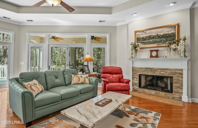 living room with crown molding, wood-type flooring, a tray ceiling, and a stone fireplace