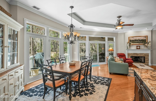 dining room with ceiling fan with notable chandelier, ornamental molding, a high end fireplace, light hardwood / wood-style floors, and a raised ceiling