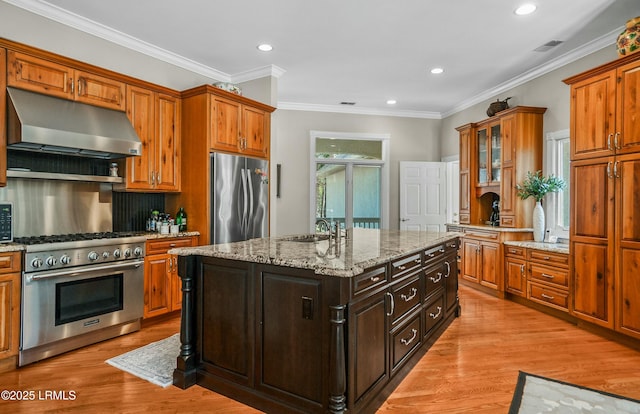 kitchen featuring extractor fan, light stone counters, light wood-type flooring, appliances with stainless steel finishes, and an island with sink