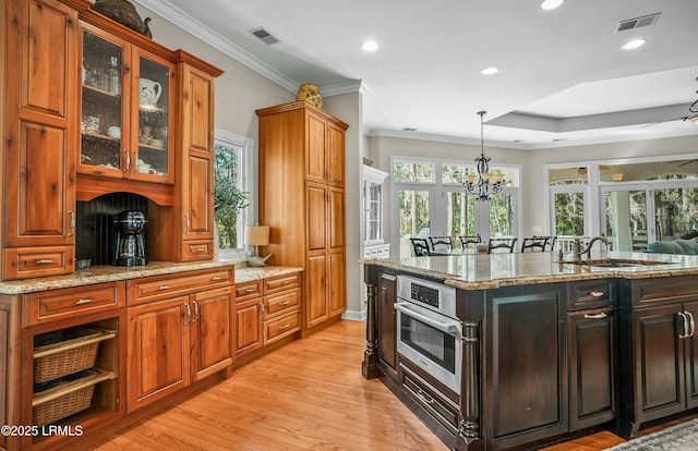 kitchen with sink, oven, light stone counters, crown molding, and light wood-type flooring