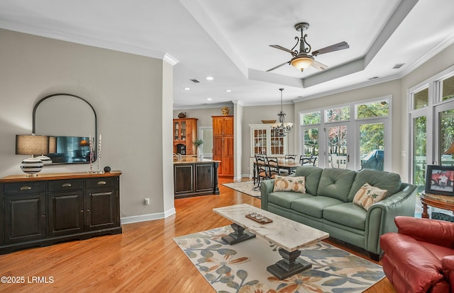 living room featuring a tray ceiling, light hardwood / wood-style flooring, ornamental molding, and ceiling fan with notable chandelier