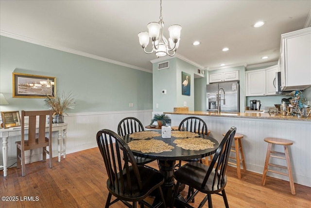 dining room with light wood-type flooring, a wainscoted wall, crown molding, and recessed lighting