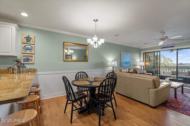 dining room with wainscoting, crown molding, light wood finished floors, and ceiling fan with notable chandelier