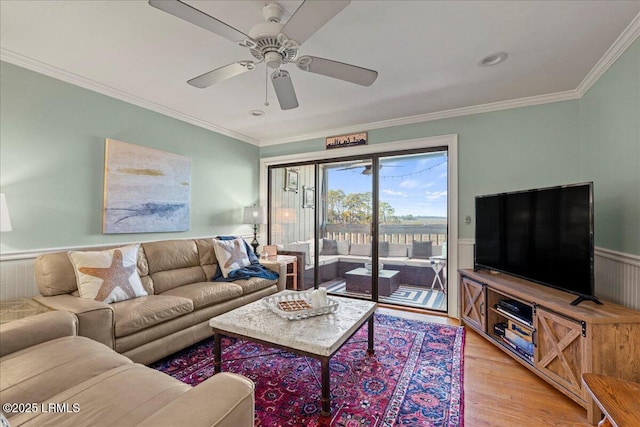 living room featuring ornamental molding, wainscoting, light wood finished floors, and a ceiling fan