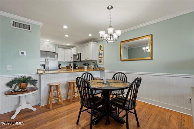 dining area with ornamental molding, a wainscoted wall, visible vents, and wood finished floors