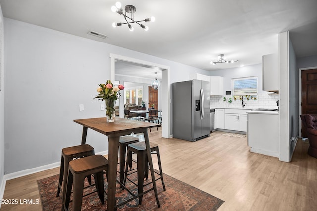 kitchen with stainless steel appliances, a chandelier, light wood-type flooring, decorative backsplash, and white cabinetry