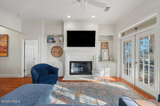 living room featuring french doors, crown molding, built in shelves, and hardwood / wood-style floors