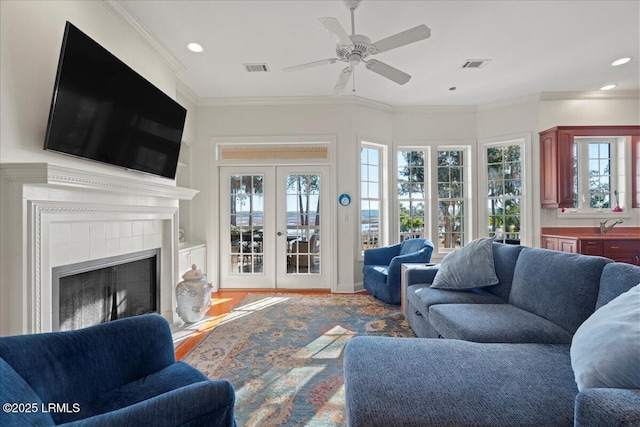 living room featuring a tile fireplace, crown molding, plenty of natural light, and french doors