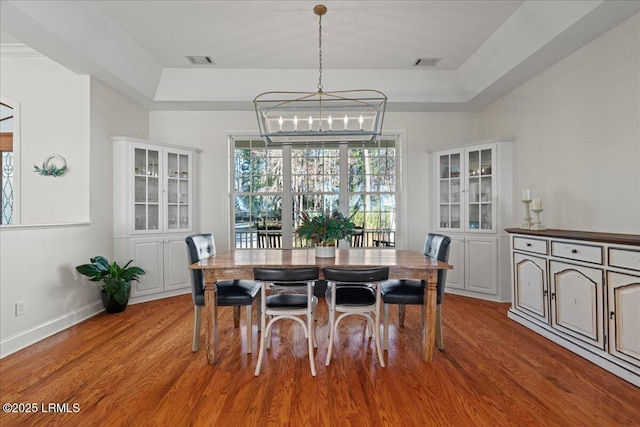 dining area featuring a notable chandelier, a tray ceiling, and light wood-type flooring