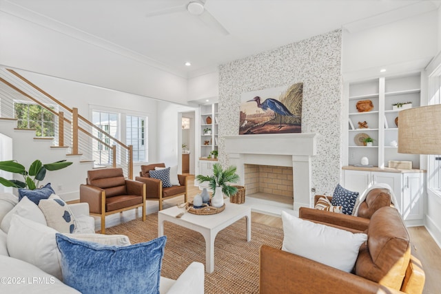 living room with light hardwood / wood-style flooring, a large fireplace, ornamental molding, built in features, and ceiling fan