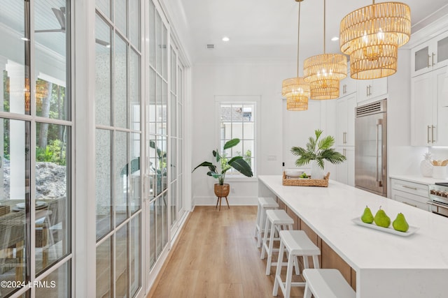 kitchen with pendant lighting, an inviting chandelier, white cabinetry, built in refrigerator, and light wood-type flooring