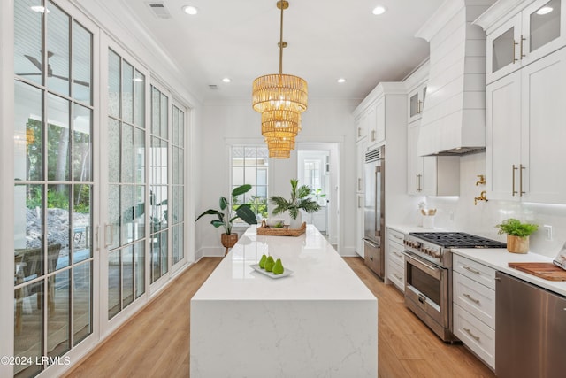 kitchen with high end appliances, custom range hood, decorative light fixtures, and white cabinetry