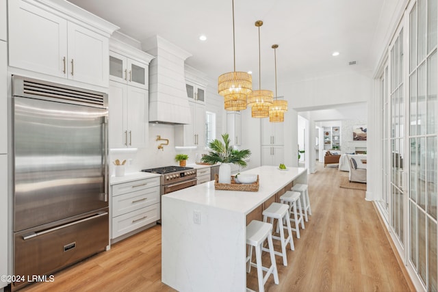 kitchen with pendant lighting, high quality appliances, white cabinets, custom exhaust hood, and light hardwood / wood-style floors