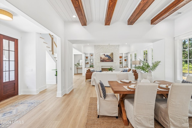 dining space featuring built in shelves, a fireplace, beam ceiling, and light hardwood / wood-style flooring