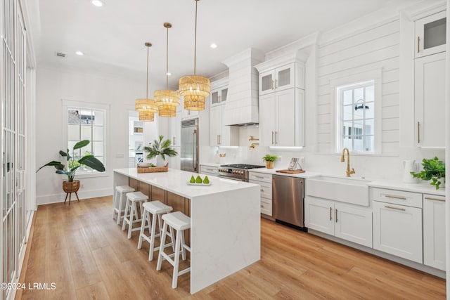 kitchen with premium range hood, hanging light fixtures, high quality appliances, a kitchen island, and white cabinets