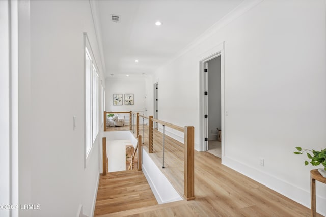 hallway featuring light hardwood / wood-style flooring, ornamental molding, and a healthy amount of sunlight