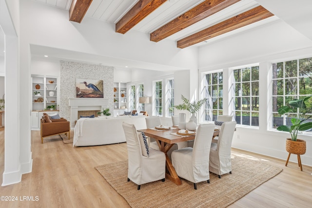 dining area featuring beam ceiling, a fireplace, built in features, and light wood-type flooring