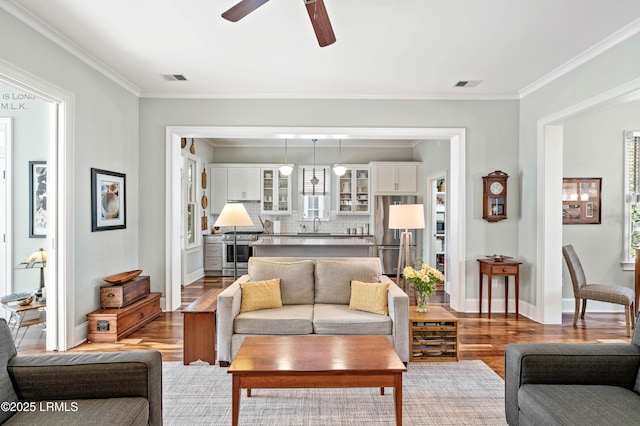 living room with a ceiling fan, wood finished floors, visible vents, and crown molding