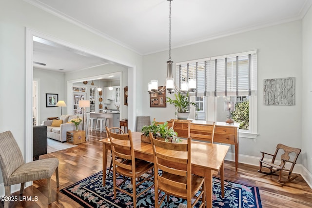 dining area featuring a notable chandelier, crown molding, baseboards, and wood finished floors