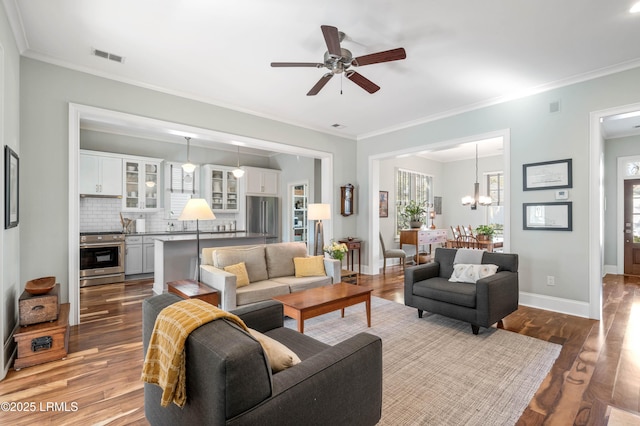 living area with baseboards, crown molding, visible vents, and wood finished floors