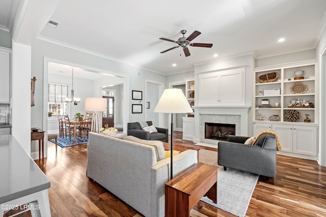 living area featuring ceiling fan with notable chandelier, a fireplace, visible vents, ornamental molding, and dark wood-style floors