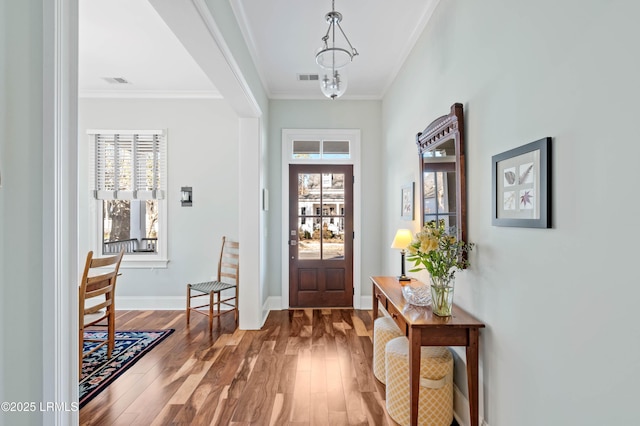 foyer entrance featuring crown molding, wood finished floors, visible vents, baseboards, and an inviting chandelier