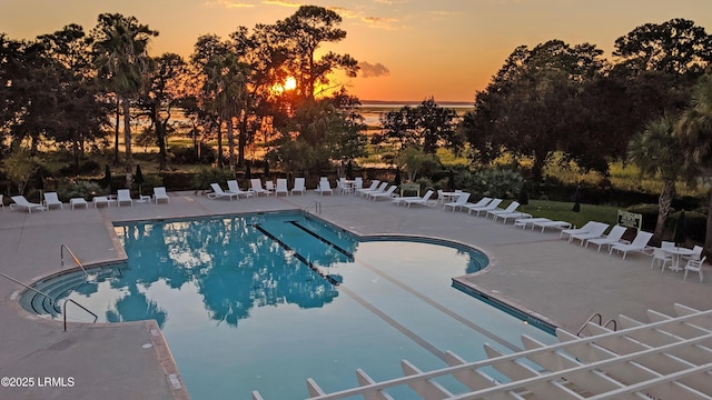 pool at dusk featuring a patio and a community pool