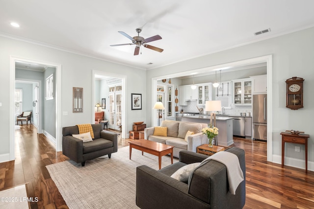 living area with ornamental molding, visible vents, baseboards, and wood finished floors