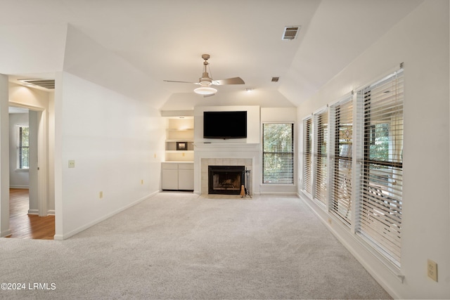 unfurnished living room with built in shelves, light colored carpet, vaulted ceiling, ceiling fan, and a tiled fireplace