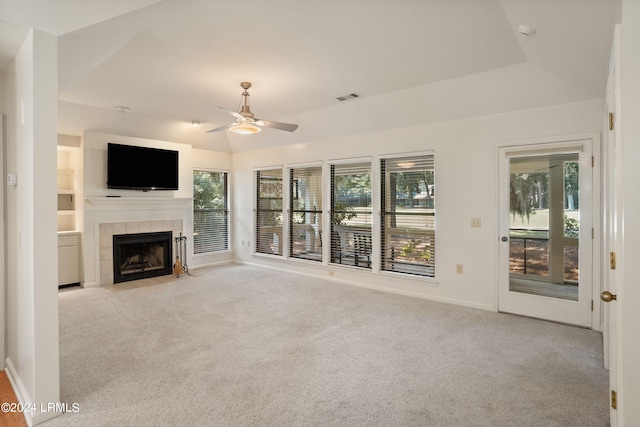 unfurnished living room with a tiled fireplace, vaulted ceiling, light carpet, and ceiling fan