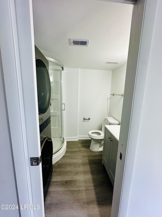 bathroom featuring toilet, an enclosed shower, vanity, hardwood / wood-style flooring, and stacked washing maching and dryer