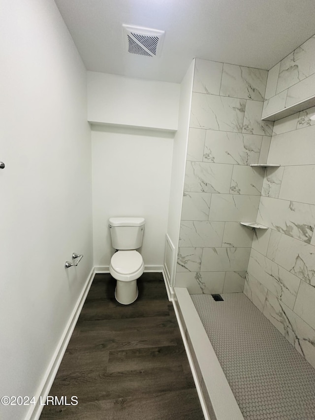 bathroom with a tile shower, wood-type flooring, and toilet