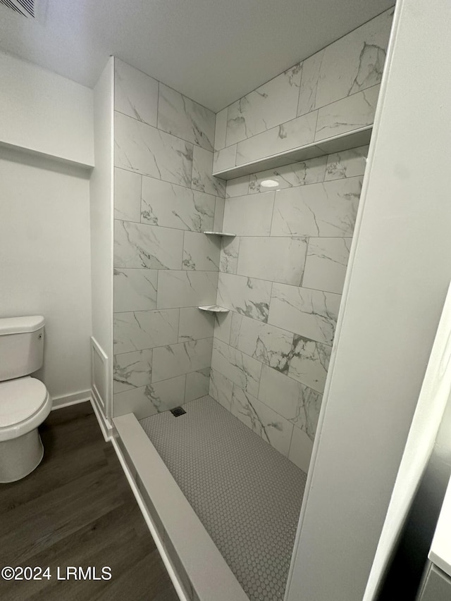 bathroom with wood-type flooring, a tile shower, and toilet