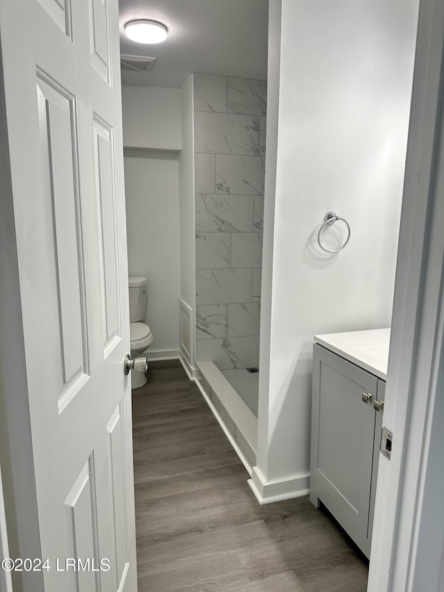 bathroom featuring a tile shower, vanity, hardwood / wood-style flooring, and toilet