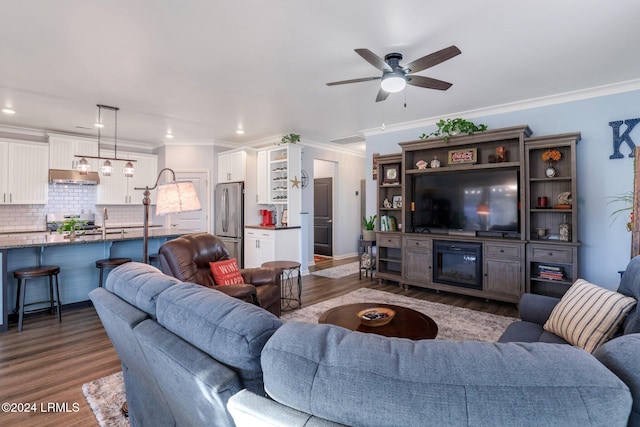 living room featuring ceiling fan with notable chandelier, dark wood-type flooring, and ornamental molding