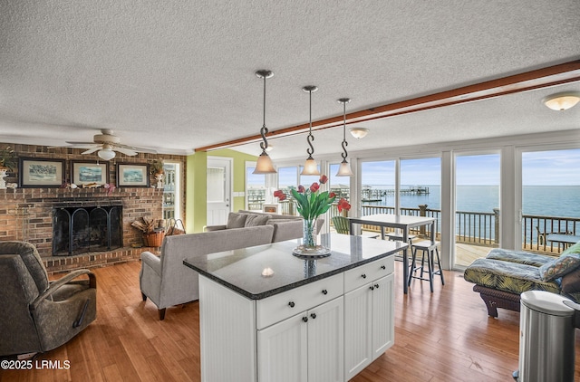 kitchen with white cabinetry, hanging light fixtures, a center island, a water view, and a fireplace