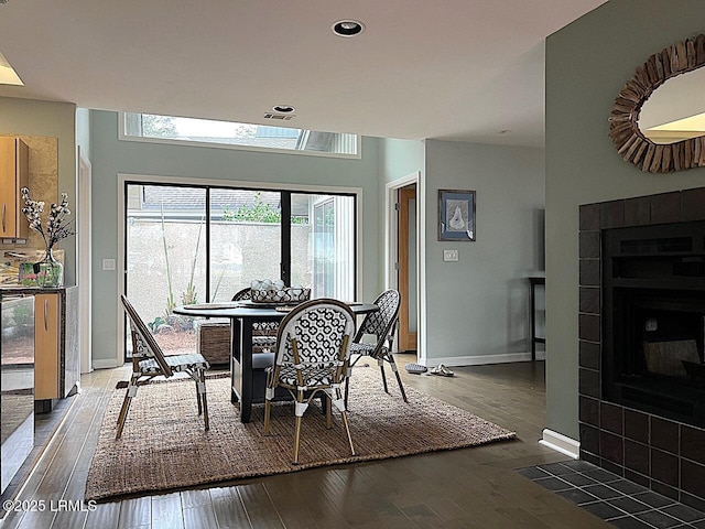 dining space with dark wood-style floors, a tile fireplace, baseboards, and recessed lighting