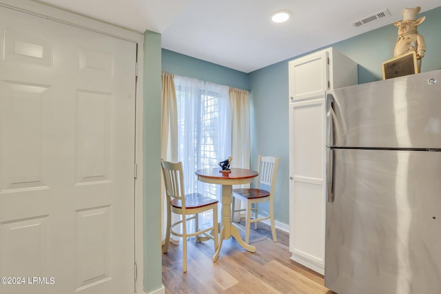 kitchen featuring stainless steel refrigerator, light wood-type flooring, and white cabinets