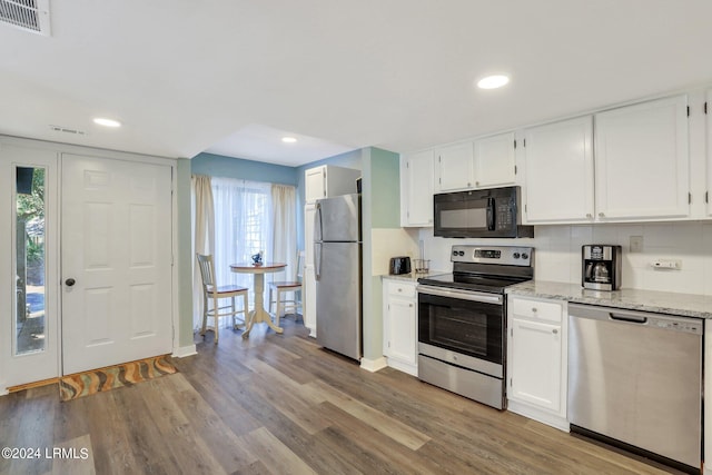 kitchen with tasteful backsplash, light wood-type flooring, appliances with stainless steel finishes, light stone countertops, and white cabinets