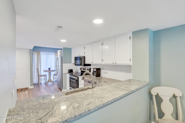 kitchen with white cabinetry, stainless steel appliances, light stone countertops, and kitchen peninsula