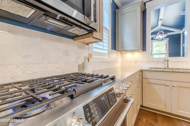 kitchen with light stone counters, dark wood finished floors, decorative backsplash, appliances with stainless steel finishes, and a sink