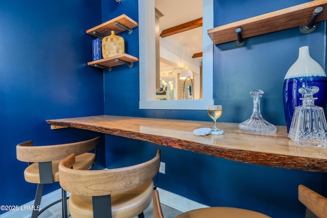 bar with a dry bar, baseboards, and beamed ceiling