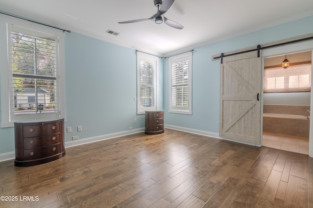 interior space featuring a barn door, wood finished floors, visible vents, baseboards, and ornamental molding