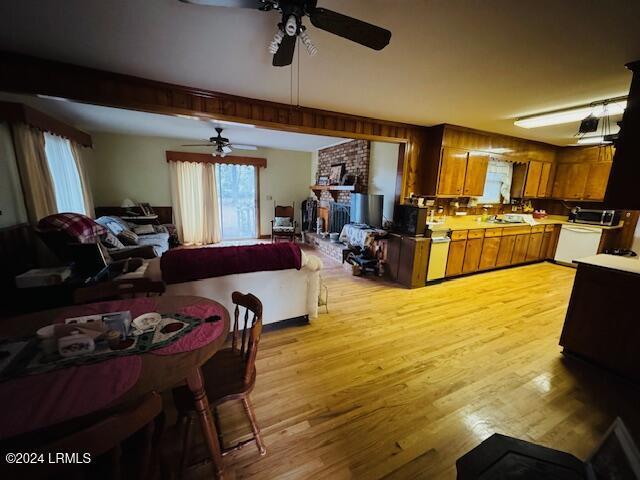 dining room with ceiling fan, a brick fireplace, and light hardwood / wood-style flooring