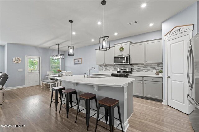 114 Danner Dr, Bluffton, SC 29909 - kitchen with stainless steel appliances, decorative backsplash, a kitchen island with sink, a kitchen bar, and light countertops